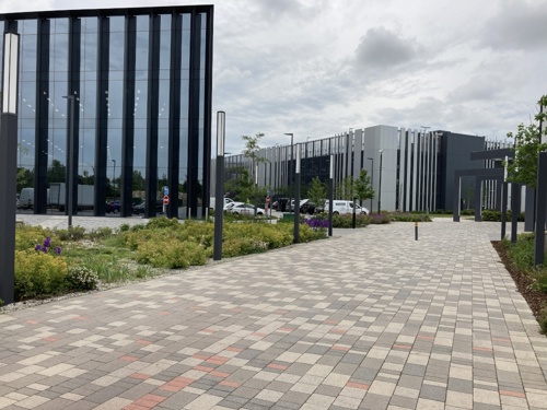 A shot of Cambridge Science Park, on the edge of the city of Cambridge. There is a brick pathway leading to some buildings.